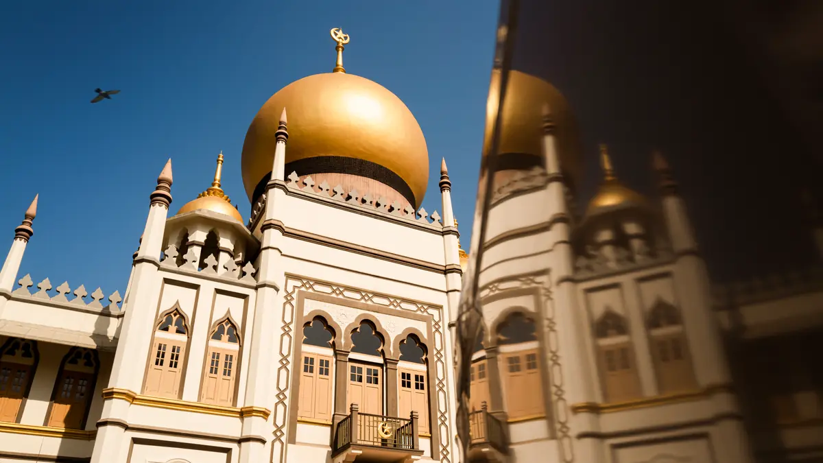 The golden dome and minarets of Sultan Mosque against a clear sky with a bird in flight