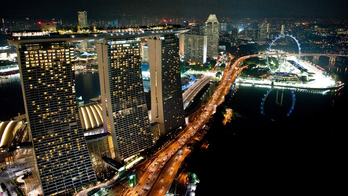 Marina Bay Sands — Aerial night view of the three Marina Bay Sands towers lit up beside Marina Bay and the Singapore Flyer